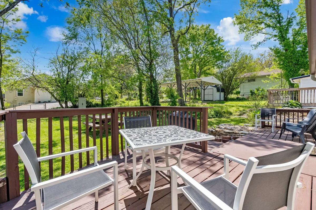 This scene showcases a furnished deck with inviting seating and a decorative table set against a backdrop of lush greenery. The space is designed for outdoor dining, social gatherings, and peaceful relaxation, fitting for sunny brunches or evening get-togethers.