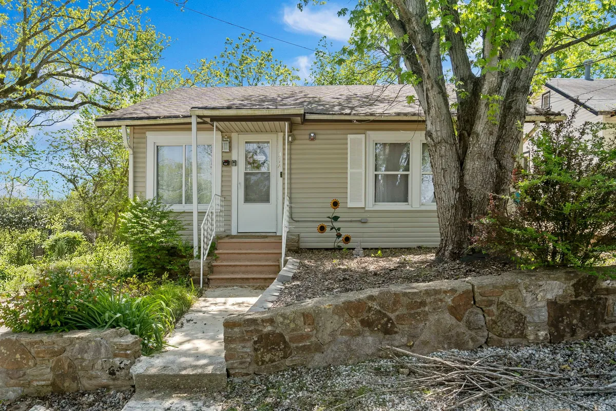 A peaceful exterior shot featuring the front door, steps, a small garden area, and mature trees. The setting feels secluded and intimate, offering a glimpse of a space perfect for quiet moments together outdoors.