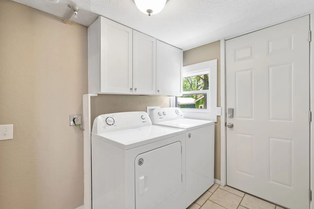 A clean, practical laundry space with a modern washer and dryer, ample storage cabinets, and a door that hints at organized household operations. The area is clutter-free and feels welcoming, emphasizing cleanliness and order.