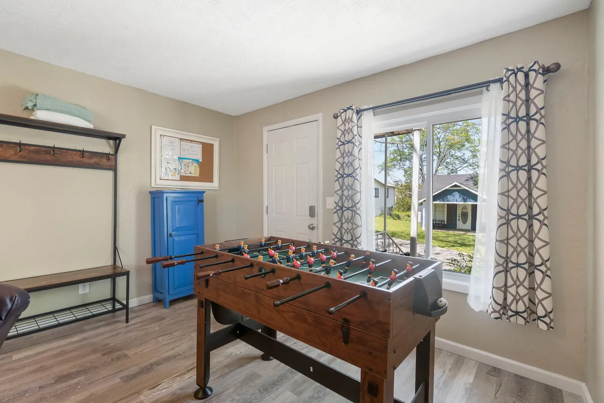 A playful, sunlit room with a foosball table, blue cabinet, and window views. The space encourages spontaneous fun and relaxation, evoking the idea of quick getaways filled with laughter and friendly competition. Natural light and open layout suggest vibrancy and flexibility in how the space is used.