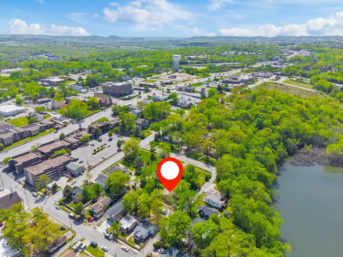 This image captures a tranquil scene of lush greenery surrounding a water body, with hints of nearby urban development. Walking paths and open spaces are visible, suggesting opportunities for outdoor exploration, biking, and fishing. The mood is peaceful, inviting families to venture out and enjoy Branson's scenic beauty and public spaces.