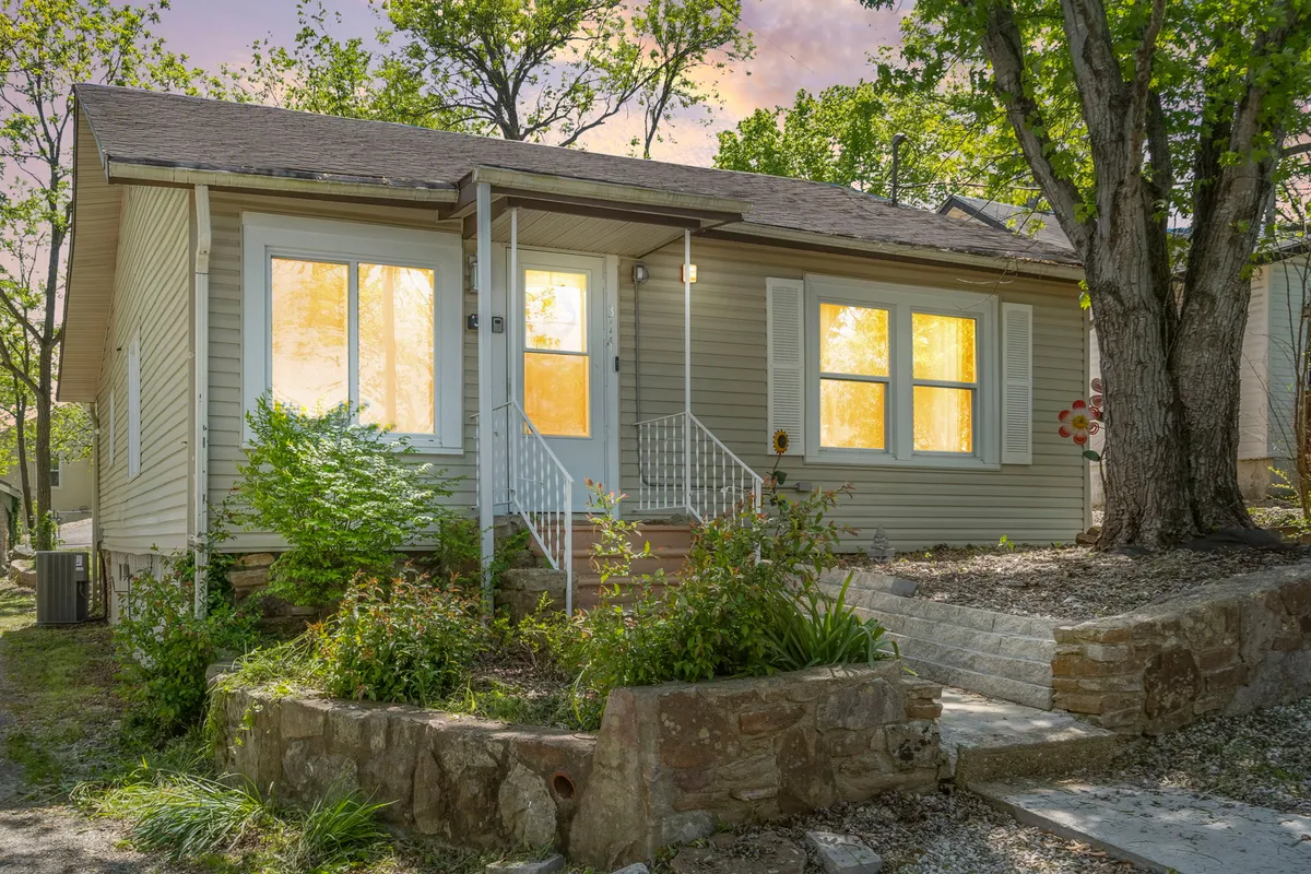 An inviting exterior view of the property, showing the front door, large windows, and carefully manicured landscaping. The steps lead to the entrance, creating a warm and welcoming first impression, while the evening lighting enhances the cozy atmosphere.