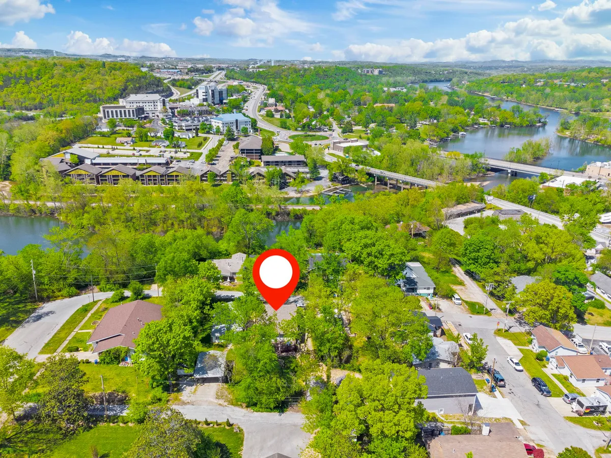 A peaceful exterior scene showcasing lush greenery, houses, a river, and roadways. People can be seen walking and biking along the scenic path that runs beside the water. The neighborhood appears vibrant, safe, and ideal for a stroll with your dog, surrounded by natural beauty and inviting outdoor spaces.