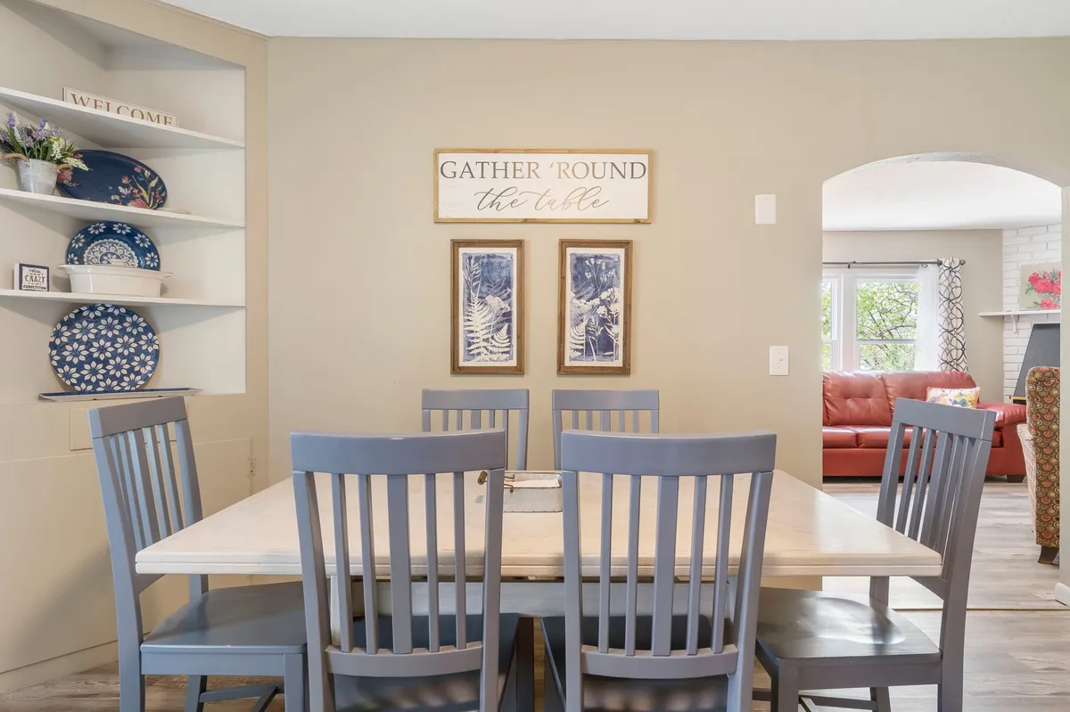 A welcoming dining space with a wooden table set for a cozy meal, framed artwork on the wall, and neatly arranged shelves with plates. The soft lighting and casual arrangement evoke an atmosphere ripe for game nights or casual family dinners.