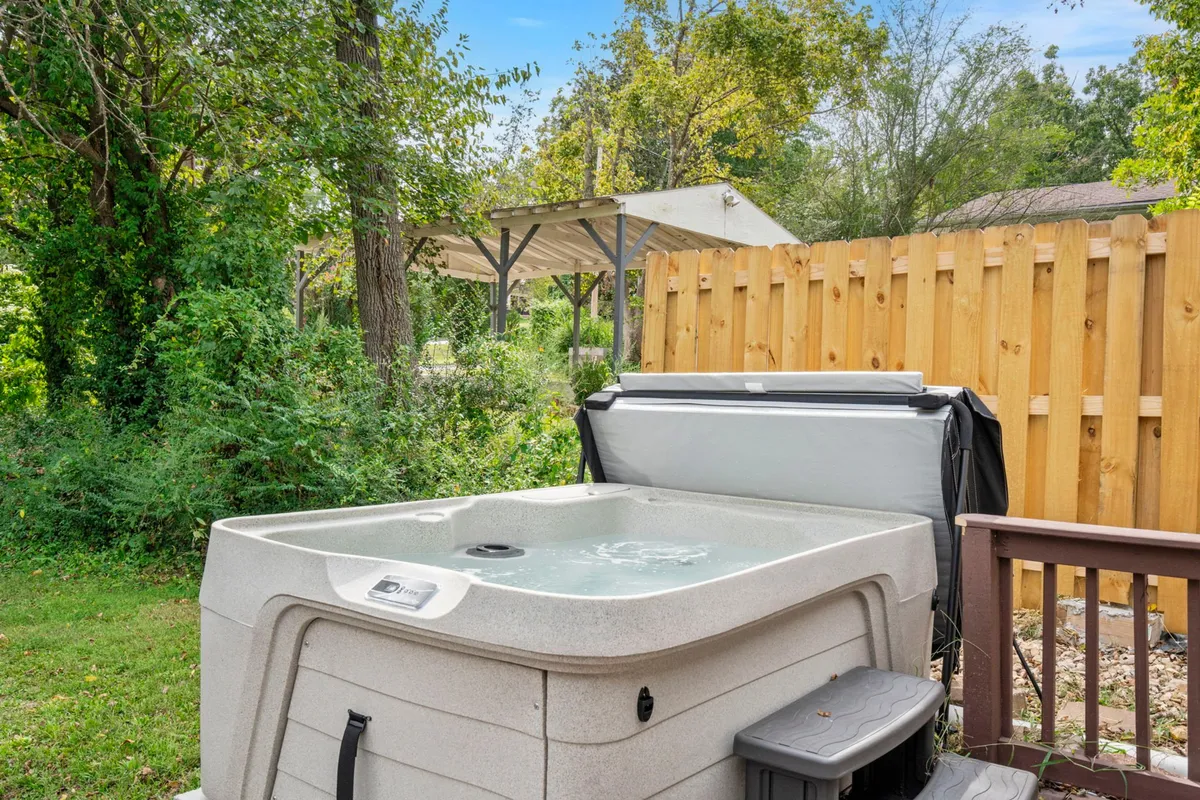 The image features a private hot tub situated in a tranquil backyard space, surrounded by lush greenery and a wooden fence. The setting offers an inviting place for relaxation after a day's adventures, with sunset and starlit possibilities creating an atmosphere of peaceful retreat.